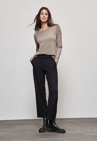 Jasnobrązowa bluzka z długim rękawem połączona z czarnymi spodniami o szerokich nogawkach i czarnymi botkami za kostkę. Materiały są gładkie, a krój luźny.