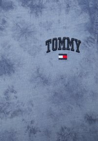 Sudadera de algodón azul tie-dye con "TOMMY" bordado en negro y un pequeño acento de bandera roja, blanca y azul debajo.