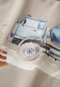 Sininen betonisekoitusauto, jossa on suuret renkaat, oranssin rakennuskohdan kartion ja lapion vieressä vaaleanbeigeä kangastaustaa vasten.