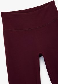 Burgunderfarbene Leggings mit hohem Bund, aus glattem Stoff, mit flachen Nähten und enganliegendem Design. Keine sichtbaren Muster oder Beschläge.