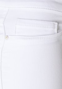 Tecido de denim branco com um bolso traseiro detalhado com um botão de metal prateado, textura suave e costuras limpas.