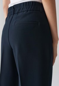 Pantalons larges bleu marine avec une taille élastique et une poche arrière unique, présentant une texture lisse et des coutures nettes.