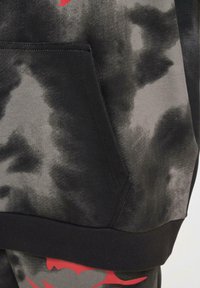 Tessuto tie-dye nero e grigio con una tasca a marsupio. Presenta un design a contrasto rosso lungo l'orlo inferiore. Texture morbida.