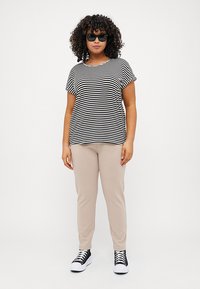 Striped black and white t-shirt, short sleeves, paired with beige pants. Model wears black sunglasses and black and white sneakers.