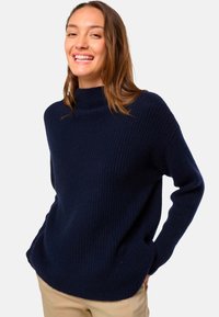 Pull en maille côtelée bleu marine avec un col haut, une coupe décontractée et des manches longues. Texture douce et fentes discrètes sur l'ourlet.