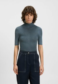 Koszulka z krótkim rękawem w fakturowanej, prążkowanej ciemnoniebieskiej tkaninie. Charakteryzuje się dopasowanym krojem i szczegółowym wykończeniem, zestawiona z spodniami o wysokim stanie w kolorze granatowym.