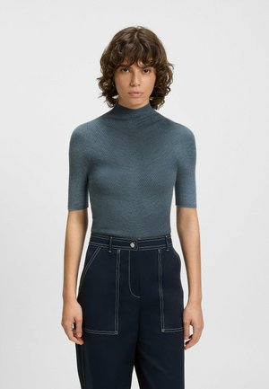 Maglia a maniche corte con collo a dolcevita in tessuto texturizzato e a coste di un blu scuro. Presenta un design aderente e cuciture dettagliate, abbinata a pantaloni blu navy a vita alta.
