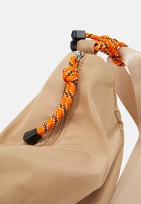 Borsa di tessuto beige con un cordino orange e nero a fantasia, dotata di chiusura a cerniera e una superficie liscia.
