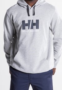 Felpa grigia con cappuccio e logo scuro "HH" e "HELLY HANSEN" sulla parte frontale, dotata di tasca a marsupio e cappuccio regolabile con cordoncino.