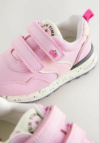 Rózsaszín sportcipők texturált felülettel, tépőzáras pántokkal, cseresznye hímzéses díszítéssel és fehér pettyes talppal.