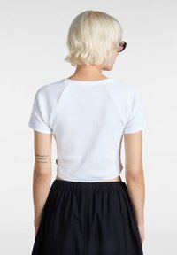 Top corto blanco de canalé con mangas cortas y un escote redondo, combinado con una falda negra de cintura elástica; tatuaje visible en el brazo.