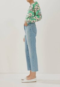 Blusa a maniche lunghe con motivo verde, jeans dritti blu chiaro a vita alta e ballerine bianche. La blusa presenta motivi floreali; i jeans sono a vita alta.