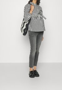 Randig långärmad skjorta i svart och vitt med knyt i midjan, tillsammans med grå slim fit-jeans och svarta slipskor med nitar. Väskan har ett vågigt mönster.