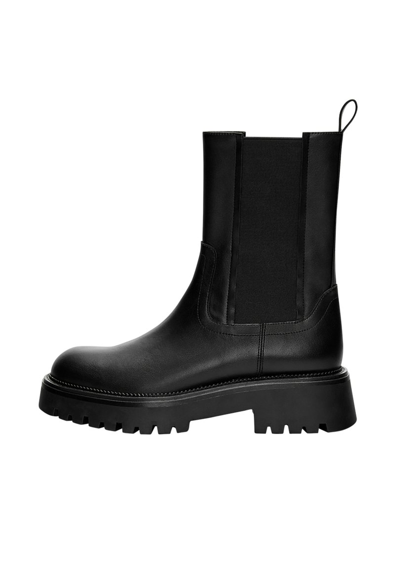 Černá kožená kotníková bota s hladkým povrchem, elastickými bočními panely a robustní podrážkou s hlubokým vzorem. Očko na zadní straně pro snadné nazouvání.