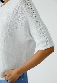 Weißer gestrickter Pullover mit kurzen Ärmeln, der ein strukturiertes Muster und einen umgeschlagenen Ärmelbund aufweist. Leichter Stoff, weich fallend und mit lässigem Schnitt.
