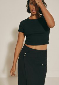 Tricou scurt cu dungi negre, asortat cu o fustă neagră cu talie înaltă, care prezintă două butoane metalice și buzunare laterale. Textura materialului este netedă.