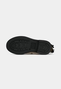 Semelle d'une botte beige avec un profil en caoutchouc noir présentant des formes de cœur et des motifs rectangulaires, taille 29, avec un détail métallique au talon.