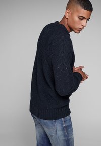 Marineblauwe kabelgebreide trui met een gestructureerd patroon, ribbels aan de mouwen en onderkant. Draag met blauwe jeans, wat een relaxte pasvorm en casual stijl toont.