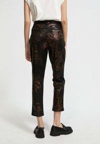 Čierne nohavice s textúrovaným hadím vzorom, so slim fit strihom a skrátenou dĺžkou. Viditeľné zadné vrecká, v kombinácii s čiernymi nazúvacími topánkami.