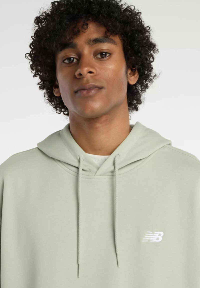 Helle grüne Kapuzenjacke aus weichem Stoff; verfügt über eine Kapuze mit Zugband und ein kleines weißes Logo auf der Brust. Strukturierte Oberfläche.