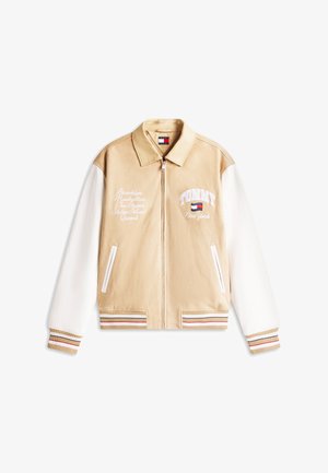 Beige-weiße Collegejacke mit Reißverschluss, gestreiften Bündchen, Vordertaschen und besticktem Schriftzug, der auf New Yorker Bezirke und das Tommy Hilfiger Logo verweist.