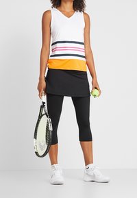 Sportig linne med vit bas och färgglada horisontella ränder i marinblått, rosa och orange; kombinerat med en svart kjol och korta leggings. Håller i ett tennisslagträ och boll.