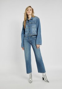 Jeansowa kurtka o kroju cropped z dwoma kieszeniami na piersiach, zestawiona z dżinsami z wysokim stanem i szerokimi nogawkami. Srebrne botki za kostkę z szpiczastymi noskami.