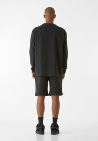 Crni dugi rukav i crne kratke hlače, izrađene od mekog materijala. Ima opušten kroj, okrugli izrez i suptilne detalje šivanja.