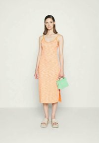 Vestido midi laranja com um padrão texturizado, alças finas, fenda lateral, combinado com uma pequena mala verde e sandálias de plataforma em bege claro.