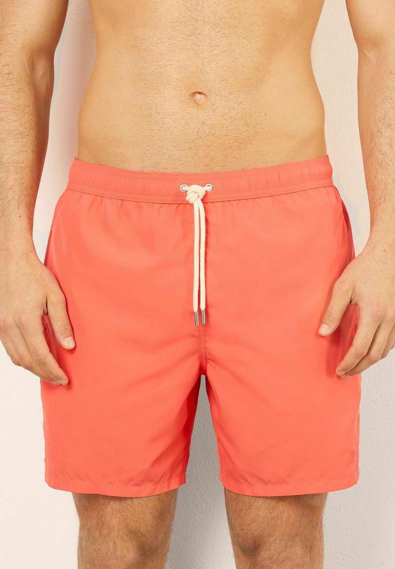 Coral swim shorts with a drawstring waistband, featuring a smooth texture and above-knee design, suitable for beachwear or pool use.