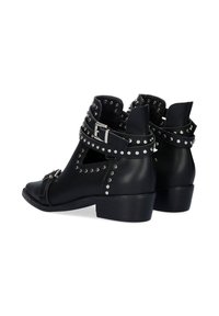 Botas de piel negra hasta el tobillo con recortes, acentos de tachuelas plateadas y correas con hebilla. Tacón bajo y detalle de superficie texturizada.