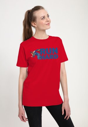 Ung kvinde med hestehale iført rød T-shirt med en fodboldspiller og fed blå tekst "LØB HÅRDT" på hvid baggrund.