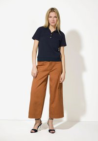 Marineblaues Poloshirt mit kurzen Ärmeln und drei Knöpfen, kombiniert mit rostfarbigen, weiten Hosen und schwarzen Zehenriemen-Heels.