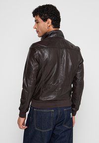 Braune Lederbomberjacke mit geripptem Saum und Kragen, die eine glatte Textur und dezente Nähdetails aufweist.