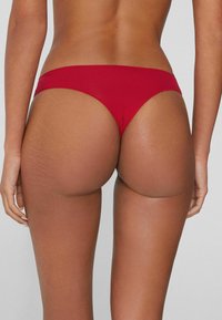 Czerwone majtki od bikini o niskim stanie i minimalnym kryciu. Gładka tkanina i czyste linie podkreślające tył.