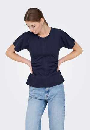 Marineblå kortærmet top med tætsiddende overdel og vidde ved kanten, lavet af bomuldsstof. Kombineret med lyseblå jeans med afslappet pasform.