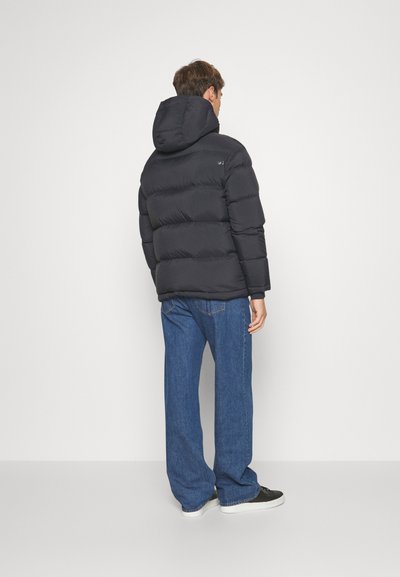 Black puffer jacket with a hood, quilted design, and a loose fit, paired with blue wide-leg jeans and black sneakers.