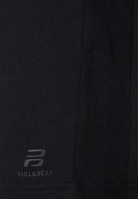 Tissu de vêtement de sport noir avec une texture côtelée. Présente un logo "PULL&BEAR" gris et un design épuré. Style simple et fonctionnel.