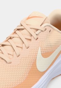 Gros plan sur une chaussure de course Nike couleur pêche avec le logo blanc Swoosh et des lacets pêche assortis sur un fond clair.