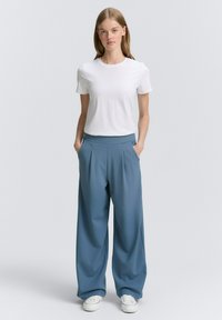 Witte kortefout t-shirt gecombineerd met losse, blauwe, geplooide broeken en witte sneakers. De stof heeft een gladde textuur en een comfortabele pasvorm.