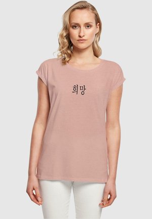 Lyserød bomulds t-shirt med rullesynede korte ærmer og rund halsudskæring, prydet med sort koreansk tekst på forsiden.
