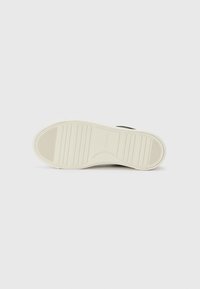 Sneaker noir avec une semelle en caoutchouc texturé, mettant en avant une semelle intermédiaire blanche. Le dessous présente des rainures horizontales pour l'adhérence.