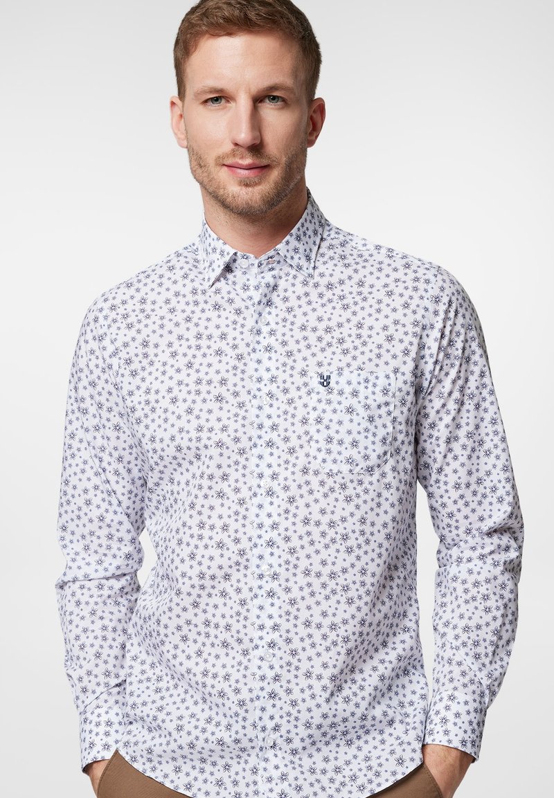 Biała koszula z długim rękawem i granatowym wzorem w kwiaty, z jedną kieszenią. Posiada miękką teksturę oraz wyprofilowany kołnierz.