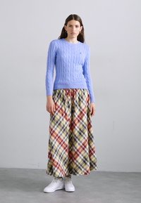 Light blue cable-knit sweater paired with a plaid maxi skirt featuring red, green, and yellow tones, complemented by white sneakers.