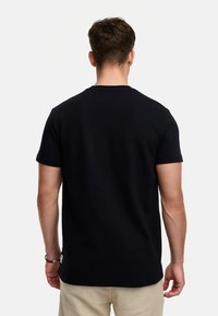 Camiseta negra de manga corta hecha de algodón. Presenta un cuello redondo, textura lisa y costuras prominentes en los hombros.