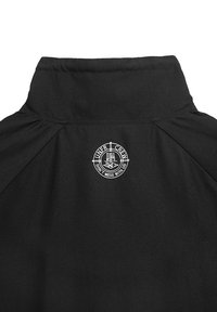 Czarna kurtka z kołnierzem, na którym znajduje się okrągły, haftowany logotyp z napisem "UNDER CREW" oraz hasłem. Gładki materiał o subtelnym połysku.