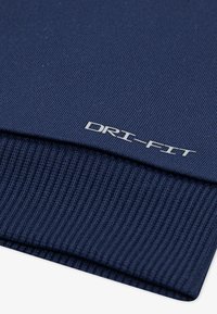 Tissu DRI-FIT bleu marine avec une texture côtelée. Le logo est en blanc, placé près de la couture, mettant en avant les matériaux de performance.