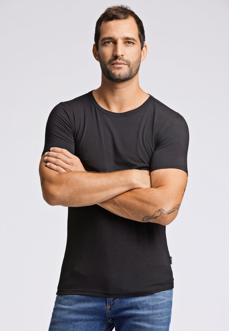 Zwarte korte mouwen t-shirt van katoen. Slim fit met een ronde halslijn en een gladde textuur. Draag met blauwe jeans, wat een eenvoudig ontwerp laat zien.