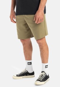 Khaki shorts made of soft fabric, featuring a relaxed fit and visible stitching. Paired with black sneakers and white logo socks.