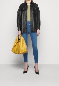 Camisa de cuero negra oversized, top verde oliva, jeans skinny azules, bolso de cuero amarillo y tacones puntiagudos negros. Diseño minimalista.